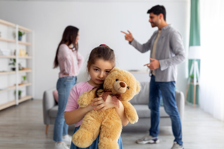 una niña sujeta su oso de peluche mientras sus padres discuten